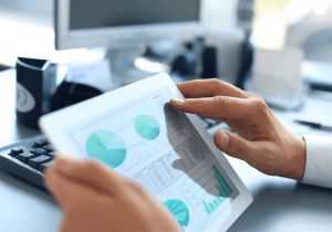 Photo of someone holding a tablet with graphs and an office environment in the background