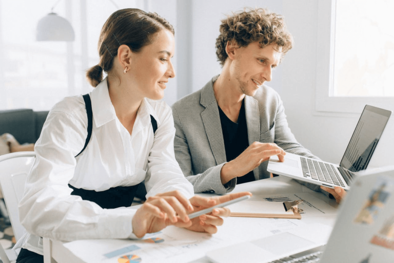 Two professionals collaborating in a modern office, using a laptop and tablet.