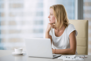 Photo of a woman using a laptop with a mug next to it