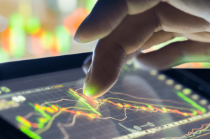 Image of a hand interacting with a touch screen showing financial graphs