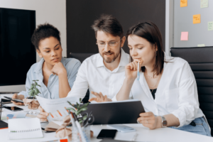 Photo of 3 people looking at a laptop screen in an office