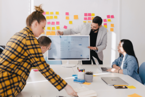 Photo of some people looking at a screen with a wall of post-its in the background