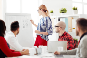 Photo of a lady pointing something on a whiteboard and others watching